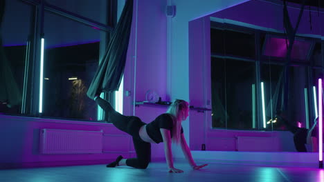 A-woman-does-yoga-and-stretching-on-a-hanging-hammock-in-neon-light.-Young-pretty-slim-body-fitness-girl-practicing-fly-yoga-in-the-gym.